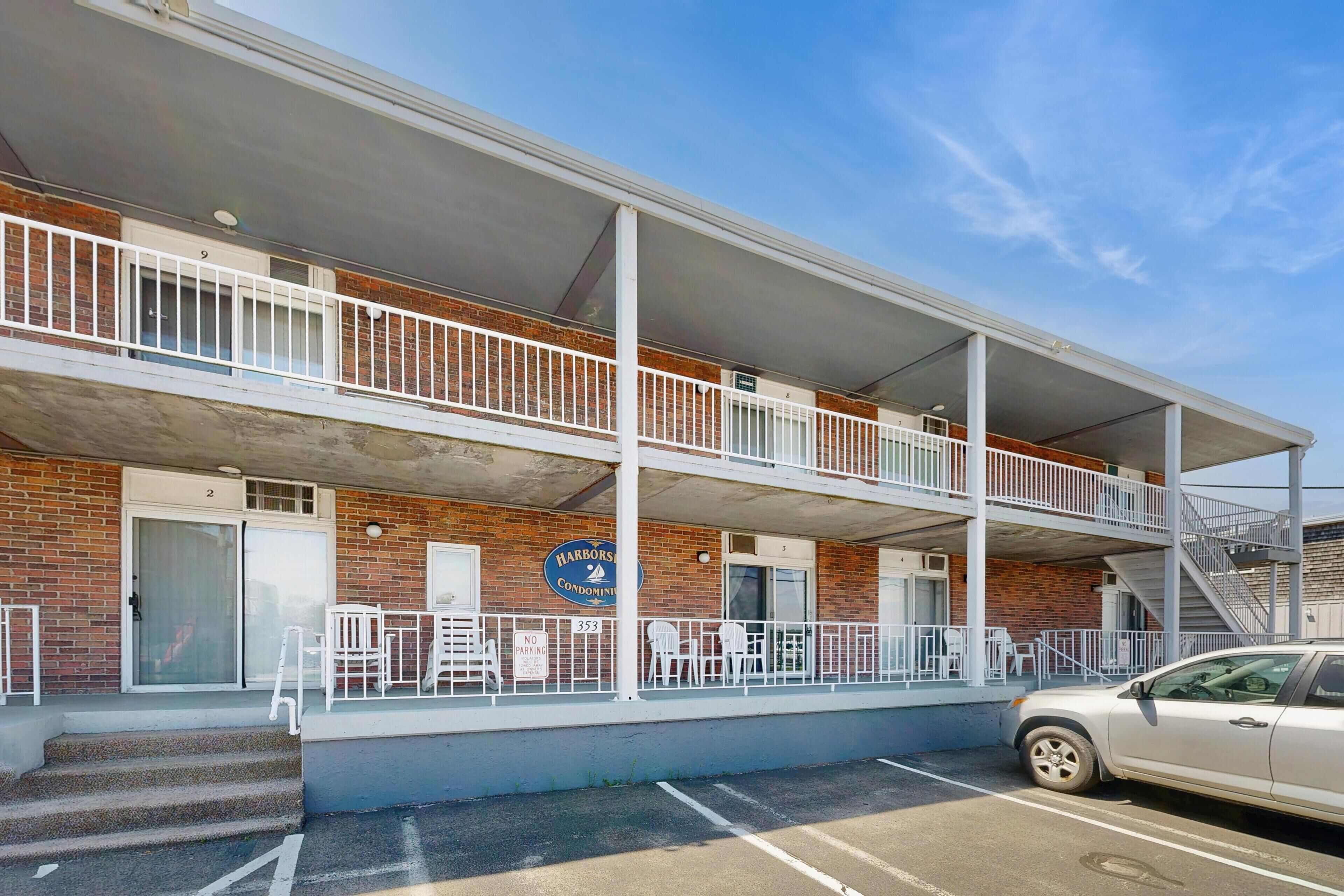 A multi-story building with a balcony, a parking area, and a sign indicating 'Harbors Condominium.'