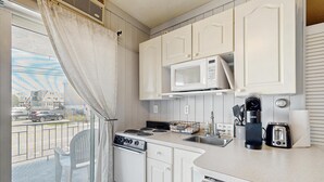 Eine kompakte Küche mit Mikrowelle, Toaster und Kaffeemaschine, einem kleinen Spülbecken und Blick auf die Straße durch ein Fenster.