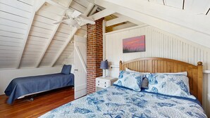A bedroom with a sloped ceiling, a brick wall, a wooden bed, and a nightstand with a lamp. - Quaint Cottage with Lobster Pot, Modern Amenities, and Several Beaches Nearby (Wells)