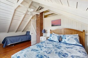 Ein Schlafzimmer mit schrägem Dach, einer Ziegelwand, einem hölzernen Bett und einem Nachttisch mit Lampe.