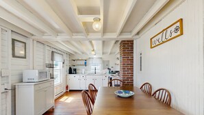 A kitchen with white cabinetry, a wooden dining table, and a 'wells' sign on the wall. - Quaint Cottage with Lobster Pot, Modern Amenities, and Several Beaches Nearby (Wells)