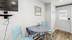 Ein Zimmer mit einem an der Wand befestigten Flachbildfernseher, einem runden Tisch mit Stühlen, einem gerahmten Bild und einer Tür mit Fenster.