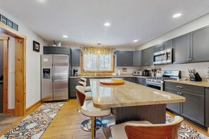 A modern kitchen with a central island, stainless steel appliances, and a patterned rug. - Two-level Townhome with Gas Fireplace, Deck, and Grill - Amazing Location (Bartlett)