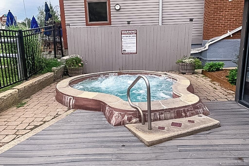 A hot tub with a wooden deck, a warning sign, and a brick wall in the background.