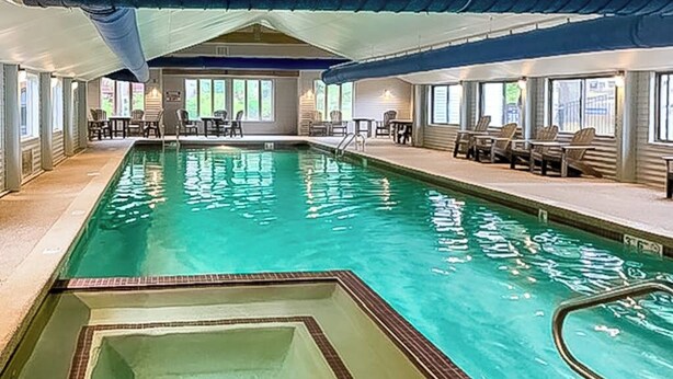Piscina interior com hidromassagem, espreguiçadeiras e área de estar coberta.
