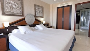 A hotel room with a large bed, two nightstands, a wooden headboard, and artwork on the walls. - Magic Balneario (Oropesa del Mar)