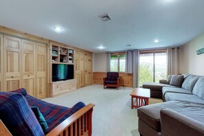 A living room with a sofa, a television, a chair, and a large window. - Mountain-view condo with deck,  W/D - close to ski/hike/shopping (Bartlett)