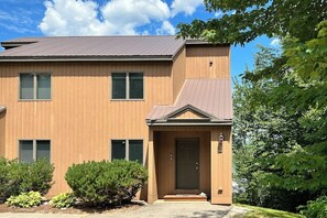 A two-story building with a brown exterior, a front entrance with a door, and a small porch area. - Mountain-view condo with deck,  W/D - close to ski/hike/shopping (Bartlett)