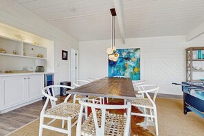 Un coin repas avec une table en bois, des chaises blanches, un luminaire suspendu et une peinture abstraite aux couleurs vives accrochée au mur.