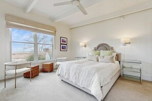 Une chambre avec un grand lit, un bureau, une chaise, des paniers en osier et une vue sur l’extérieur.