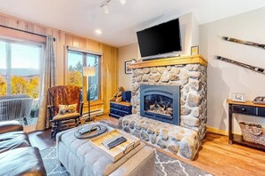 Ein gemütliches Wohnzimmer mit Kamin aus Naturstein, einem Flachbildfernseher und einem Skiständer an der Wand.