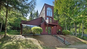 Una casa moderna con veranda in vetro, terrazza in legno e una scala che conduce a un balcone.