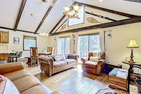 Ein geräumiges Wohnzimmer mit Holzböden, einem großen Sofa, einem kleineren Sessel und einem Essbereich mit Tisch und Stühlen.