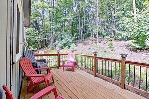 Eine Holzterrasse mit Adirondack-Stühlen, einem kleinen Tisch und Blick auf einen Wald.