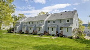 Reihenweise gebaute eingeschossige Häuser mit schrägem Dach, einem gepflegten Rasen und einem Gewässer im Hintergrund.