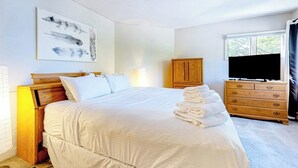 Ein Schlafzimmer mit einem Bett, einer Holzkommode, einem Fernseher und einem Fenster.