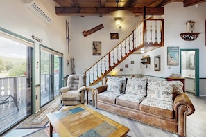 A spacious living room with a wooden staircase, a sofa with patterned cushions, a fur armchair, and a wooden coffee table. - Convenient Townhouse plus Loft w/Free WiFi, Full Kitchen, Gas Fireplace, & More (Bartlett)
