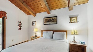 Ein Schlafzimmer mit Holzboden, einem Bett mit weißer Bettwäsche, zwei Nachttischen mit Lampen und Wanddekorationen.