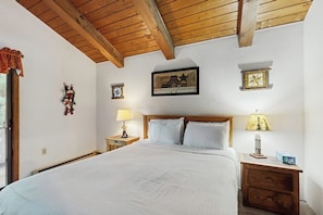 A bedroom with a wooden ceiling, a bed with white bedding, two bedside tables with lamps, and wall decorations. - Convenient Townhouse plus Loft w/Free WiFi, Full Kitchen, Gas Fireplace, & More (Bartlett)