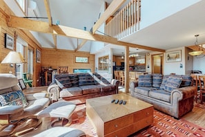 A spacious living area with wooden beams, a sofa set, a coffee table, and a staircase leading to an upper level. - Charming retreat + loft w/deck, gas grill, private washer/dryer, and jetted tub (Bartlett)