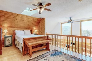 A bedroom with a wooden bed, a nightstand, a ceiling fan, and a view of the outdoors. - Charming retreat + loft w/deck, gas grill, private washer/dryer, and jetted tub (Bartlett)