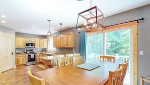 A modern kitchen with wooden cabinets, a dining table, and a large window. - Chic home with game room, fireplace & mountain view - near Story Land & skiing (Bartlett)