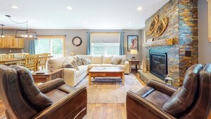 A living room with a fireplace, leather chairs, a sofa, a coffee table, and a dining area with wooden furniture. - Chic home with game room, fireplace & mountain view - near Story Land & skiing (Bartlett)