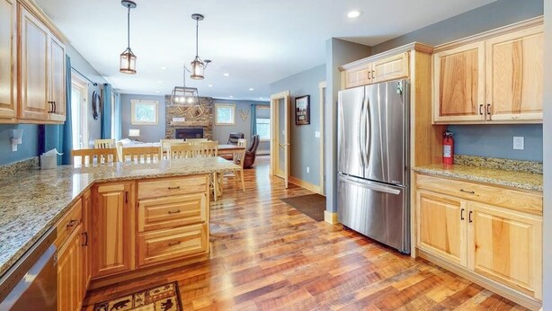 A spacious kitchen with wooden cabinets, a large island, stainless steel appliances, and pendant lighting. - Chic home with game room, fireplace & mountain view - near Story Land & skiing (Bartlett)