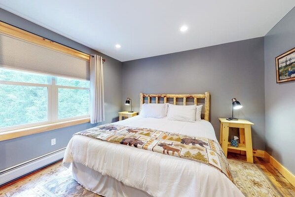 A bedroom with a large bed, two bedside tables, a window with blinds, and a painting on the wall. - Chic home with game room, fireplace & mountain view - near Story Land & skiing (Bartlett)