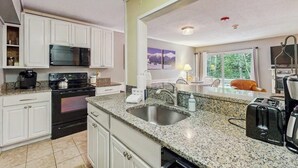 A kitchen with white cabinets, a granite countertop, a stainless steel sink, a toaster, and a microwave.
