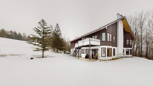 Une maison à deux étages avec un balcon, un escalier et un paysage enneigé.