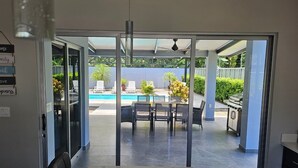 A view through a glass door into a patio area with a pool, outdoor furniture, and a grill. - Villa Malicamich - Tropical Escape (Puntarenas Province)