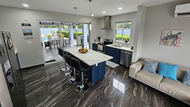 A modern kitchen with a central island, bar stools, and a dining area with a view. - Villa Malicamich - Tropical Escape (Puntarenas Province)