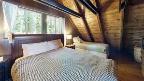 Ein Schlafzimmer einer Holzhütte mit einem großen Bett, einem kleineren Bett und einem Fenster mit Vorhängen.