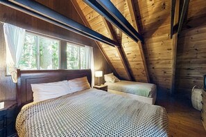 Ein Schlafzimmer einer Holzhütte mit einem großen Bett, einem kleineren Bett und einem Fenster mit Vorhängen.