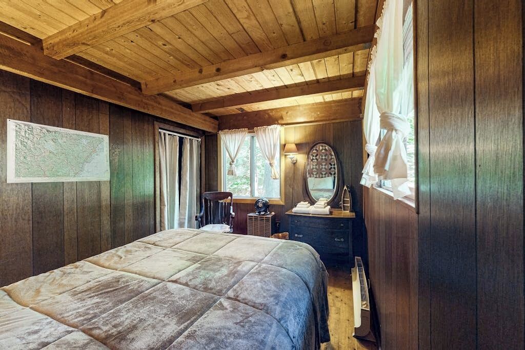 A wooden-paneled bedroom with a bed, a dresser, a mirror, and a map on the wall.