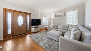 Un salón con puerta de madera, televisor, sofá gris y alfombra.