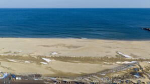 Una playa con cielo despejado, orilla de arena y un área cercada con construcciones.