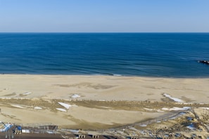 Ein Strand mit blauem Himmel, sandigem Ufer und einem eingezäunten Bereich mit Gebäuden.