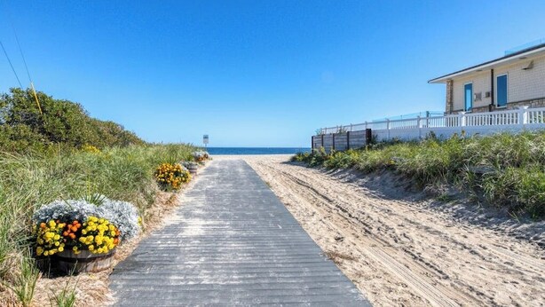 Un sentier côtier menant à une plage, avec un bâtiment sur la droite et un ciel dégagé.