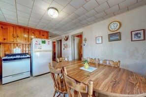 A kitchen with wooden cabinets, a stove, a refrigerator, a dining table with chairs, and wall-mounted clocks.