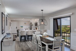 A modern kitchen with white cabinetry, a dining area with white chairs, and a large sliding glass door to the outdoors.