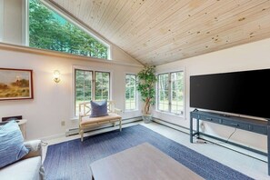 A spacious living room with a large TV, a bench, and a potted plant. - White Mountain Glen | House in Bartlett with hot tub, sauna, firepit & game room (Bartlett)