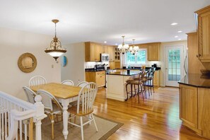 A kitchen with wooden cabinets, a dining table with chairs, and a central island with stools. - White Mountain Glen | House in Bartlett with hot tub, sauna, firepit & game room (Bartlett)