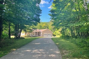 A two-story house with a garage, surrounded by trees and a paved driveway. - White Mountain Glen | House in Bartlett with hot tub, sauna, firepit & game room (Bartlett)