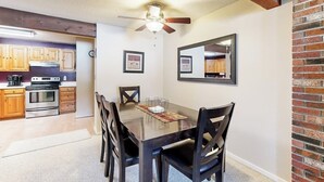 A dining area with a wooden table, four chairs, a ceiling fan, and a kitchen in the background. - Snowbird-friendly home with heated pool, sauna, game room, tennis, BBQ, W/D (Bartlett)