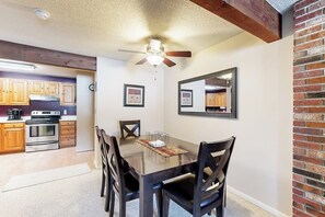 A dining area with a wooden table, four chairs, a ceiling fan, and a kitchen in the background. - Snowbird-friendly home with heated pool, sauna, game room, tennis, BBQ, W/D (Bartlett)