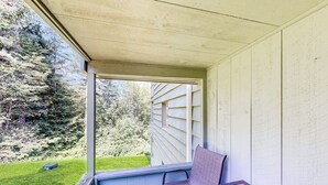A covered porch with a table and chair, a view of a green lawn, and a house in the background. - Comfort, convenience & amenities: close to skiing, hiking & shopping (Bartlett)