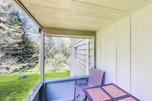 A covered porch with a table and chair, a view of a green lawn, and a house in the background. - Comfort, convenience & amenities: close to skiing, hiking & shopping (Bartlett)