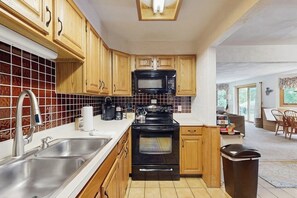 A kitchen with wooden cabinets, a black microwave, a stainless steel sink, and a trash can. - Dog-Friendly Condo with Patio, Full Kitchen, W/D, & Free WiFi (Bartlett)
